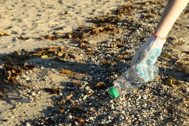 Photo of Woman picking up plastic bottle outdoors, closeup. Space for text