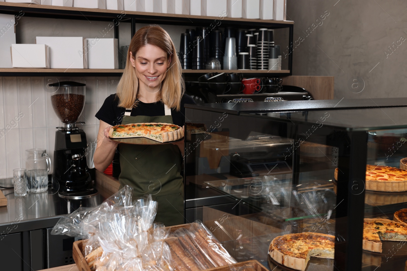 Photo of Happy seller holding delicious quiche at cashier desk in bakery shop