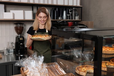 Happy seller holding delicious quiche at cashier desk in bakery shop