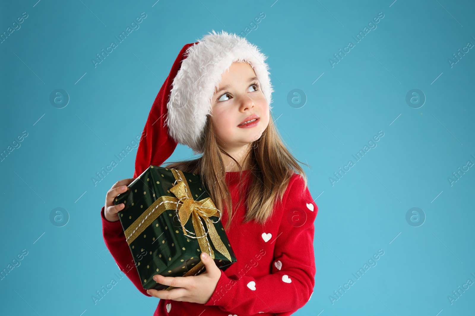 Photo of Cute child in Santa hat with Christmas gift on light blue background