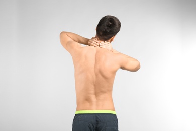 Young man suffering from neck pain on light background