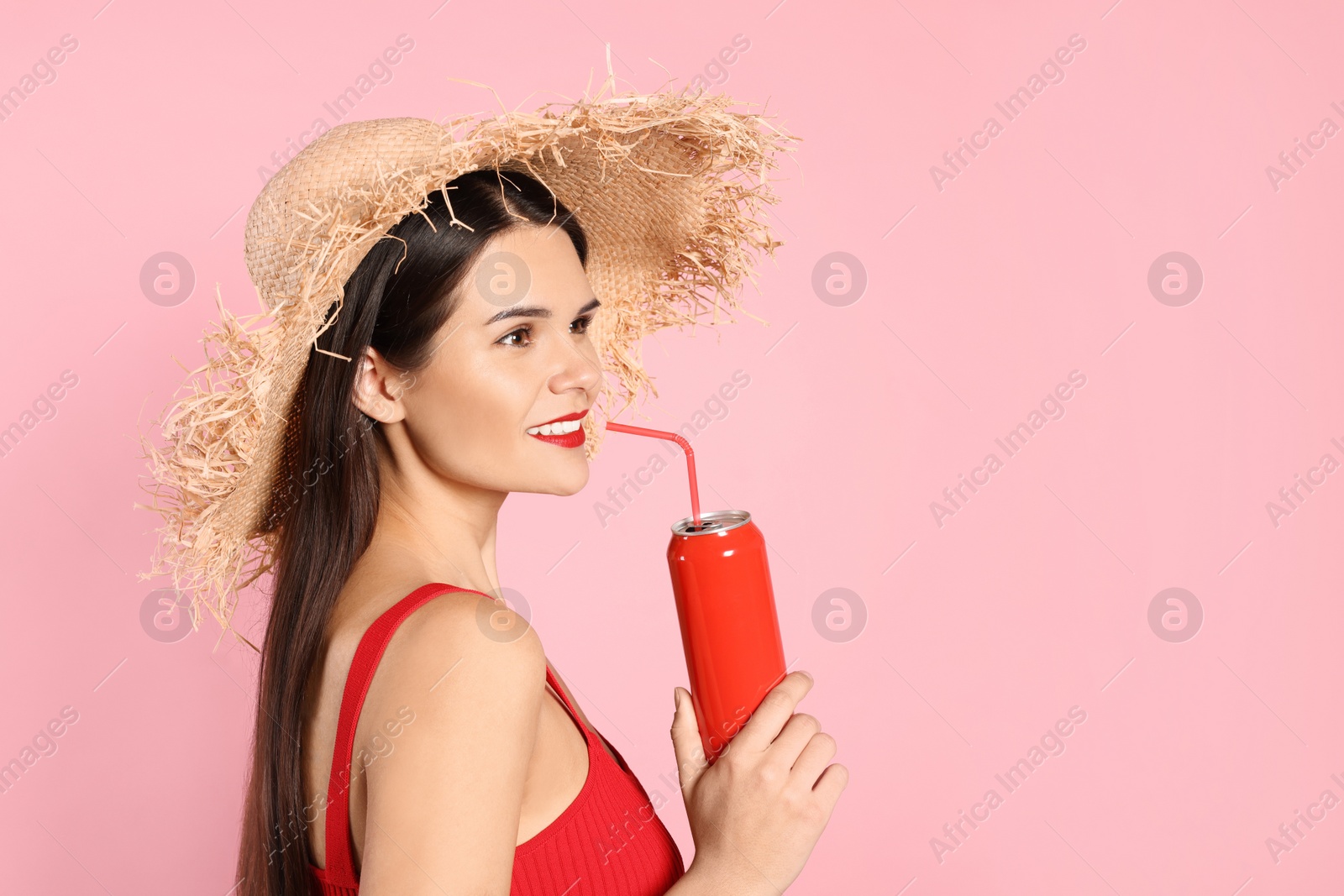 Photo of Beautiful young woman with straw hat drinking from tin can on pink background. Space for text