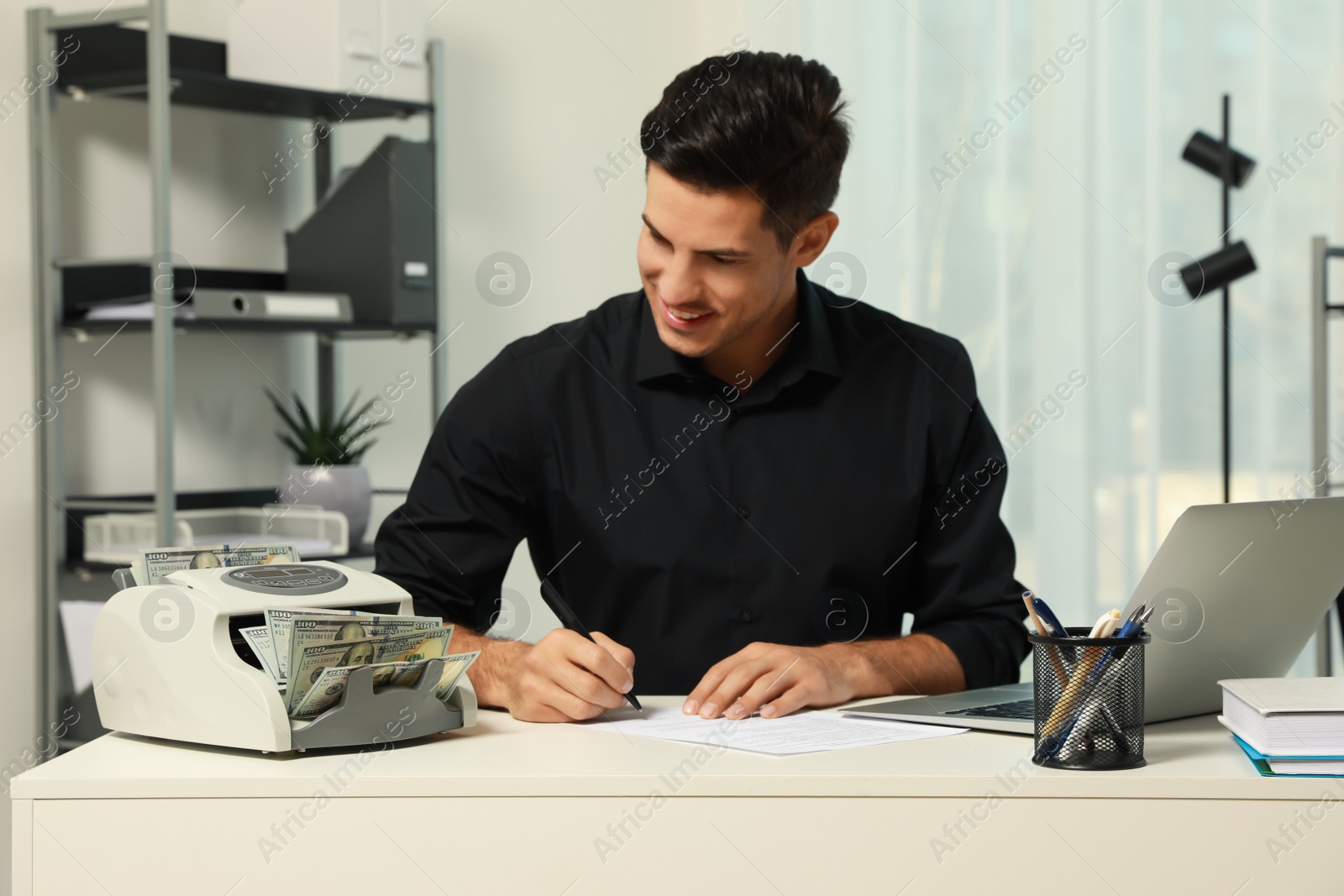 Photo of Man using banknote counter at white table indoors