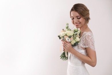 Young bride with elegant hairstyle holding wedding bouquet on white background