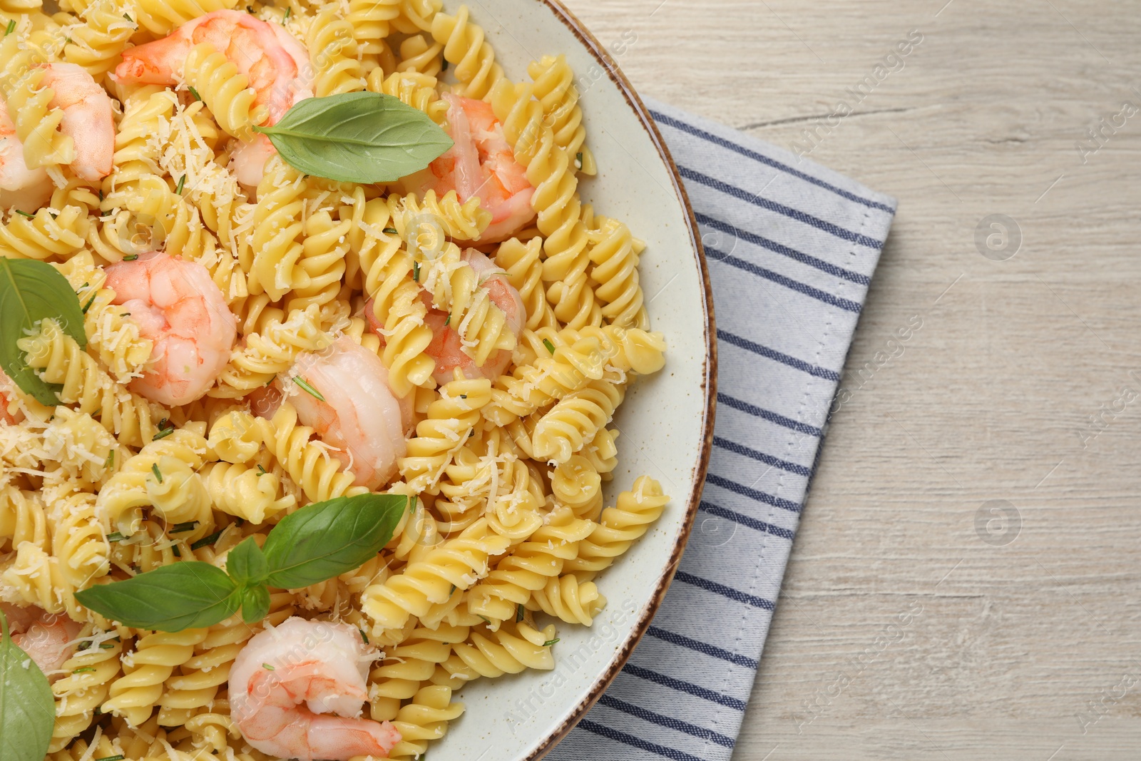 Photo of Plate of delicious pasta with shrimps, basil and parmesan cheese on light wooden table, top view. Space for text