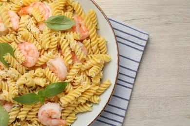 Plate of delicious pasta with shrimps, basil and parmesan cheese on light wooden table, top view. Space for text