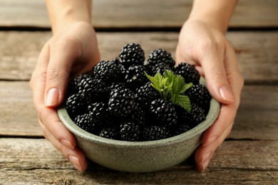 Photo of Woman putting bowl of fresh ripe black blackberries on wooden table, closeup