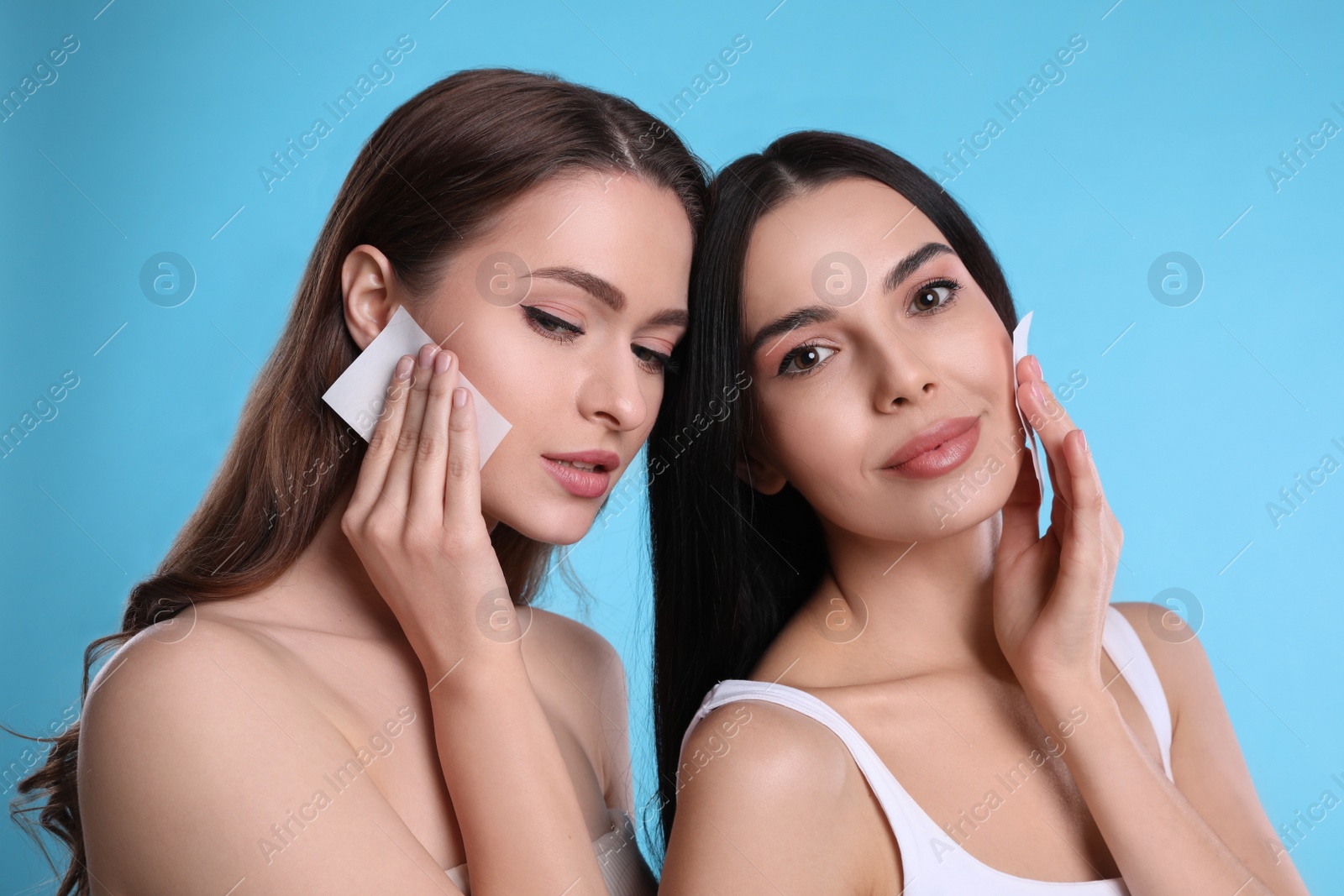 Photo of Beautiful women using mattifying wipes on light blue background