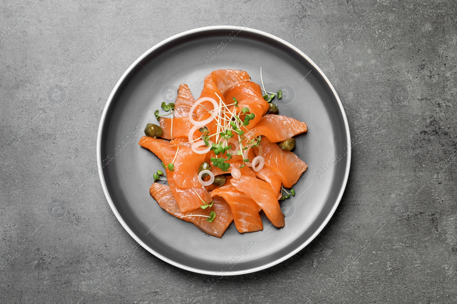 Photo of Salmon carpaccio with capers, onion and microgreens on grey table, top view