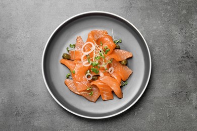 Salmon carpaccio with capers, onion and microgreens on grey table, top view