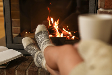 Woman with cup of hot cocoa near fireplace indoors, closeup