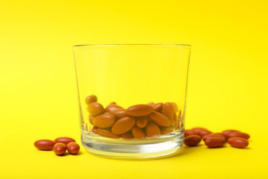 Photo of Glass with pills on yellow background, closeup. Anemia treatment