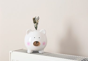 Piggy bank with money on heating radiator against light background