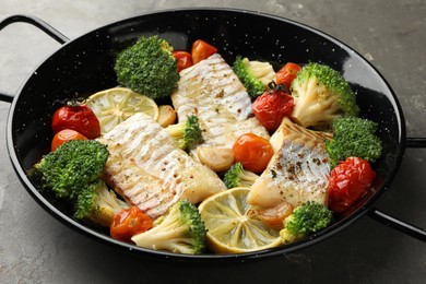 Photo of Tasty cod cooked with vegetables in frying pan on grey table