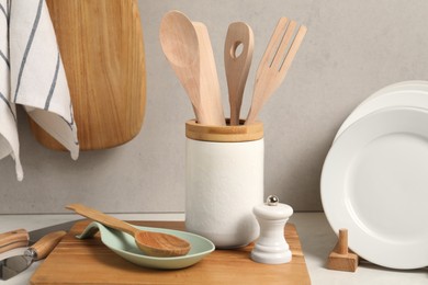 Set of different kitchen utensils and plates on white near gray wall
