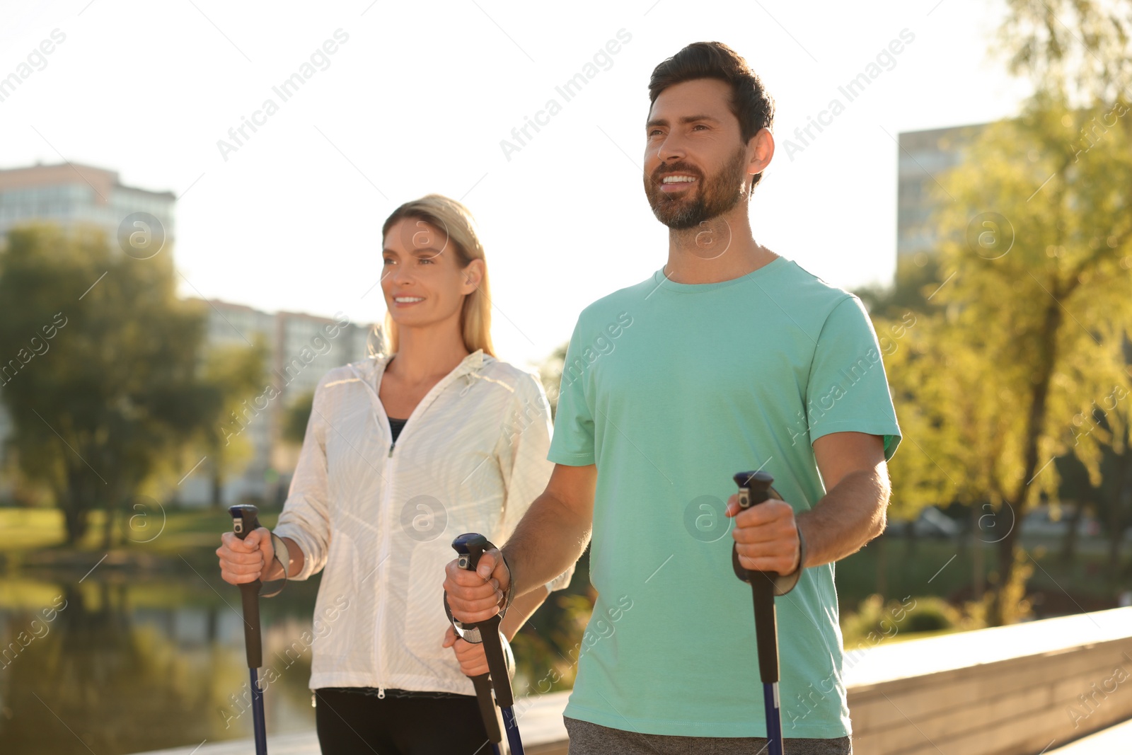 Photo of Happy couple practicing Nordic walking with poles outdoors on sunny day