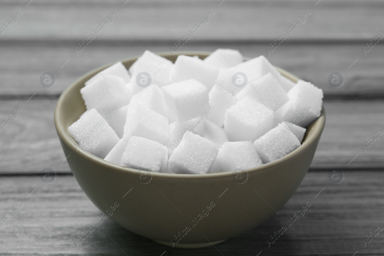 Photo of White sugar cubes in bowl on wooden table, closeup