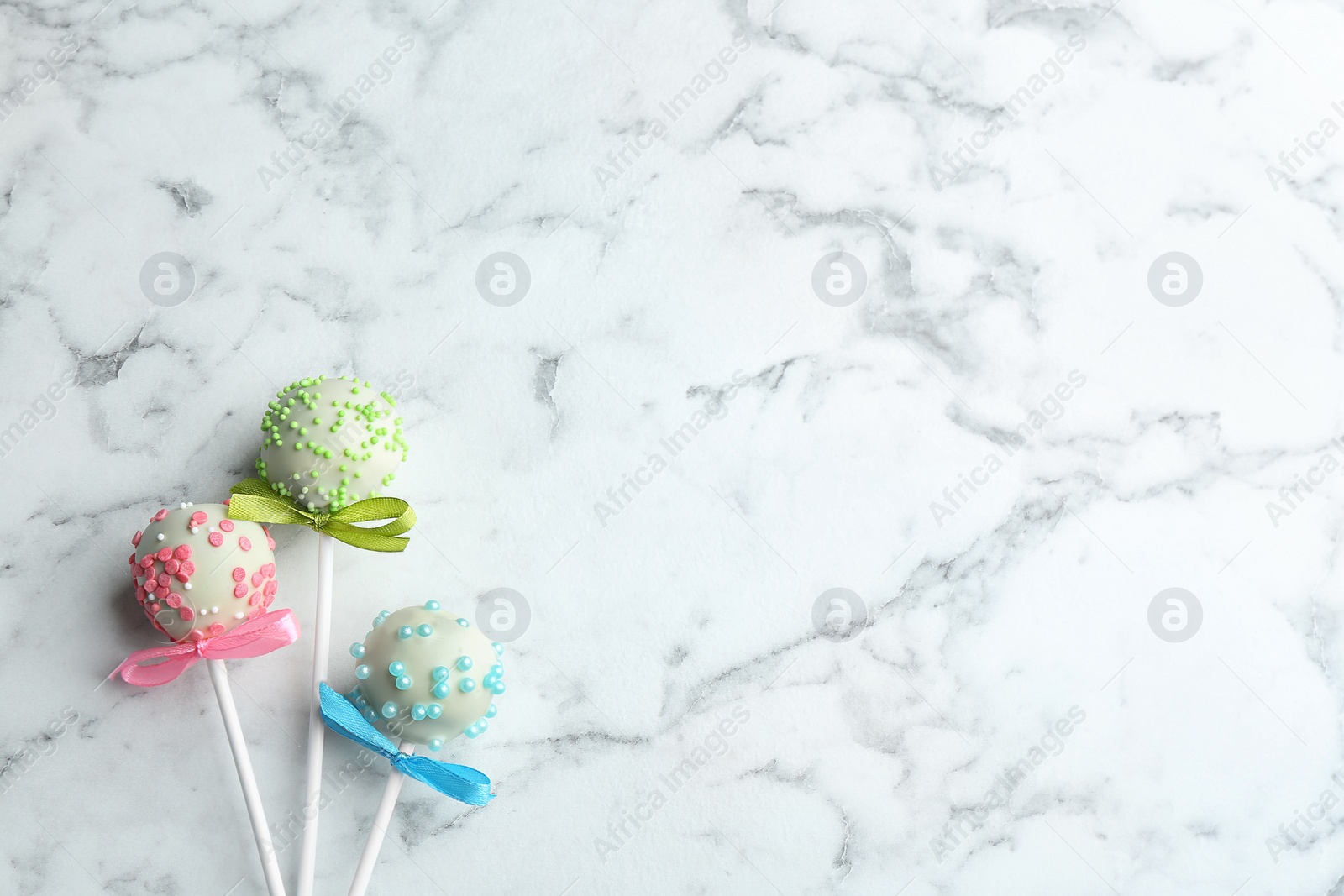 Photo of Different tasty cake pops on white marble background, flat lay. Space for text