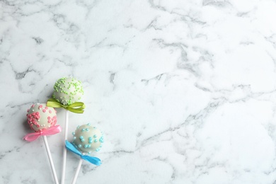 Different tasty cake pops on white marble background, flat lay. Space for text