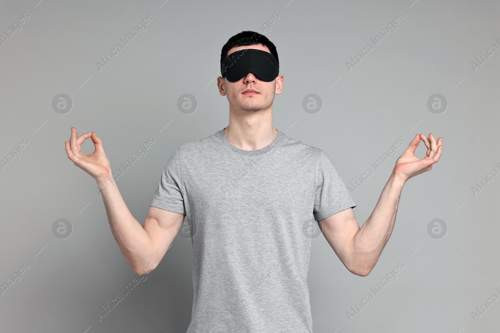 Photo of Man in pyjama and sleep mask meditating on grey background