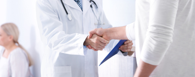 Doctor and patient shaking hands in hospital hall, closeup. Banner design