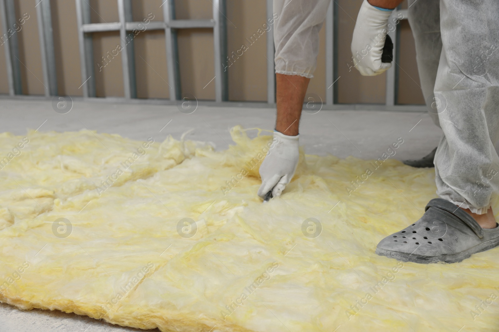 Photo of Worker cutting insulation material indoors, closeup. Space for text