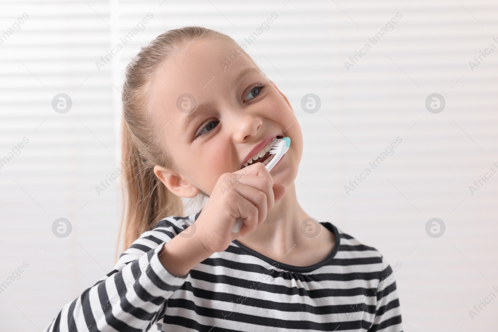Photo of Cute little girl brushing her teeth with plastic toothbrush on white background