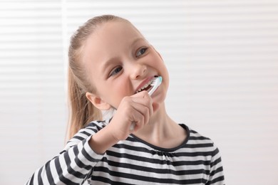 Cute little girl brushing her teeth with plastic toothbrush on white background