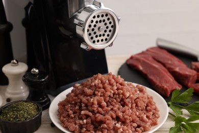 Photo of Electric meat grinder with beef, spices and parsley on white wooden table