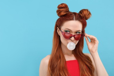 Photo of Beautiful woman in sunglasses blowing bubble gum on light blue background. Space for text