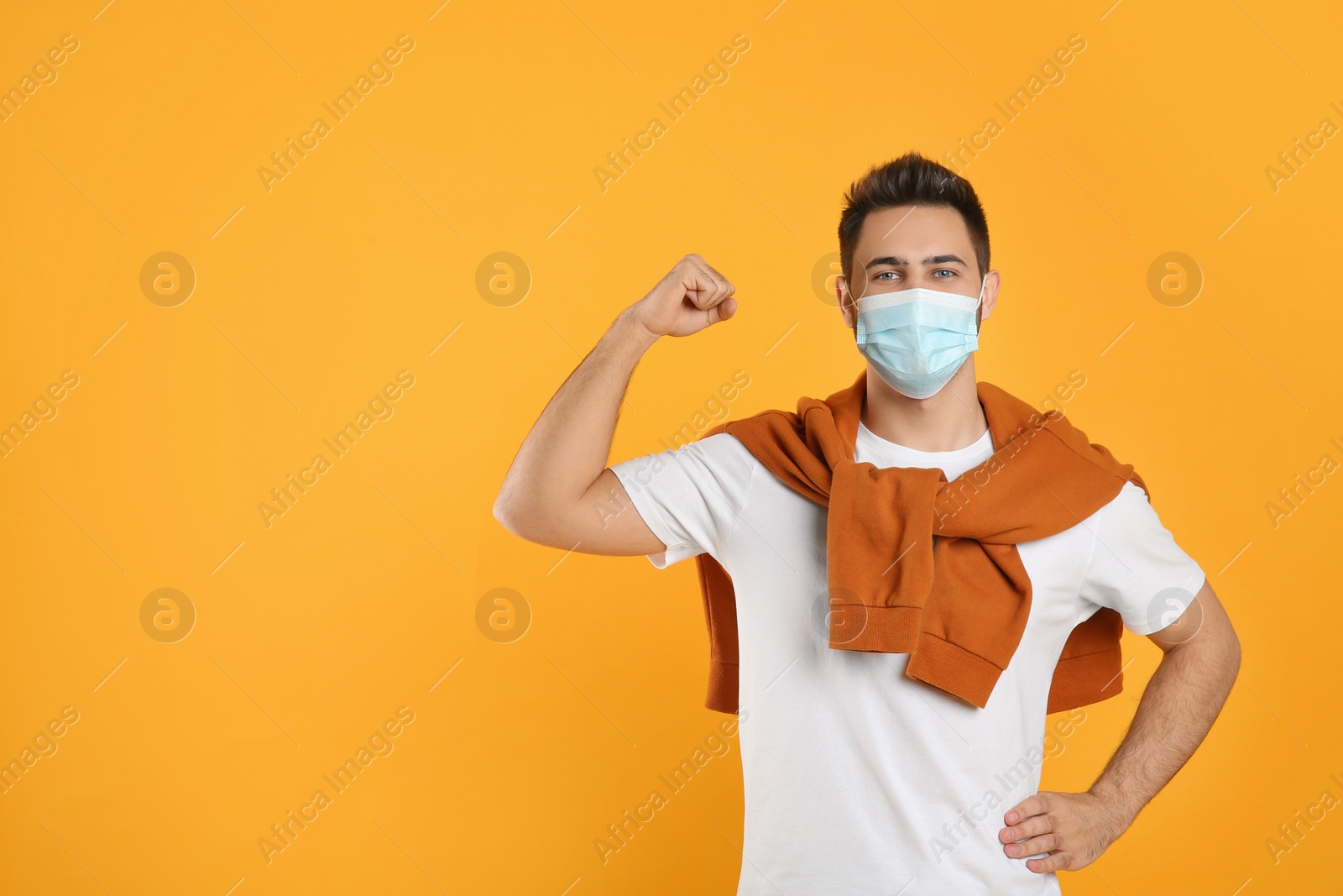 Photo of Man with protective mask showing muscles on yellow background, space for text. Strong immunity concept