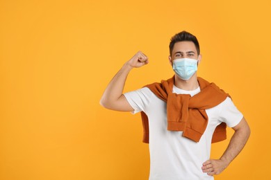 Photo of Man with protective mask showing muscles on yellow background, space for text. Strong immunity concept