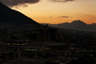 Picturesque view of sunset with dark clouds above big mountains and city
