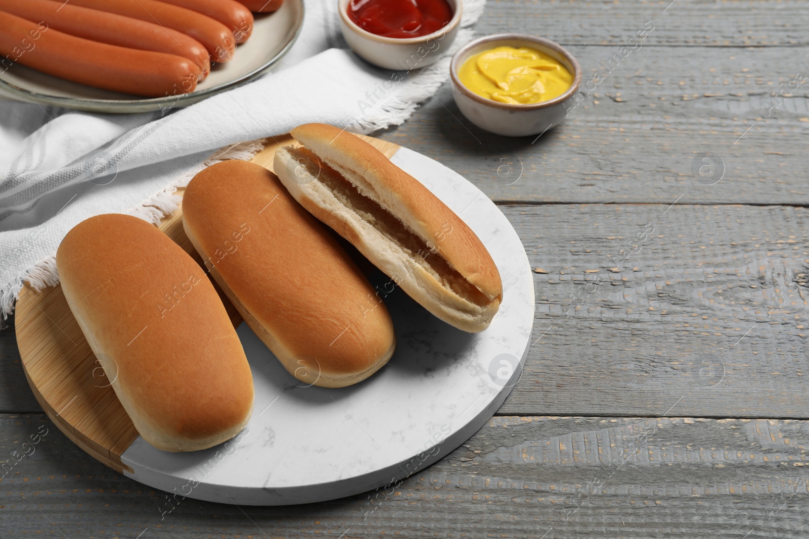 Photo of Tasty fresh buns and different ingredients for hot dog on light grey wooden table, space for text