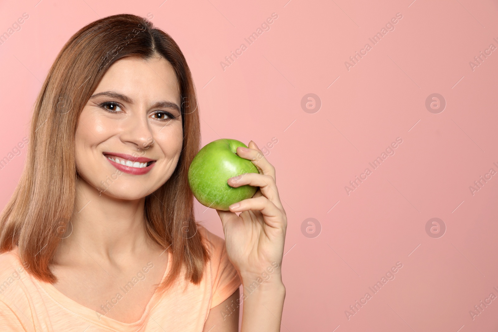 Photo of Smiling woman with perfect teeth and green apple on color background. Space for text