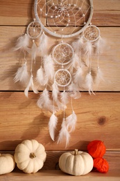 Photo of Beautiful dream catcher, white pumpkins and calyces of physalis near wooden wall