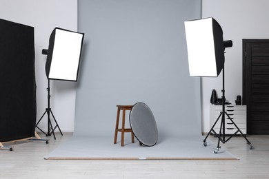 Photo of Stool with light reflector surrounded by professional lighting equipment in photo studio