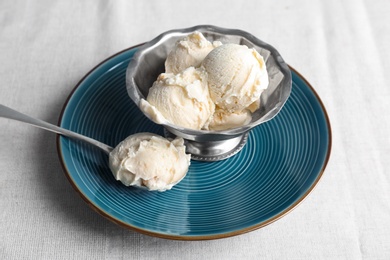 Photo of Bowl and spoon with tasty vanilla ice cream on fabric