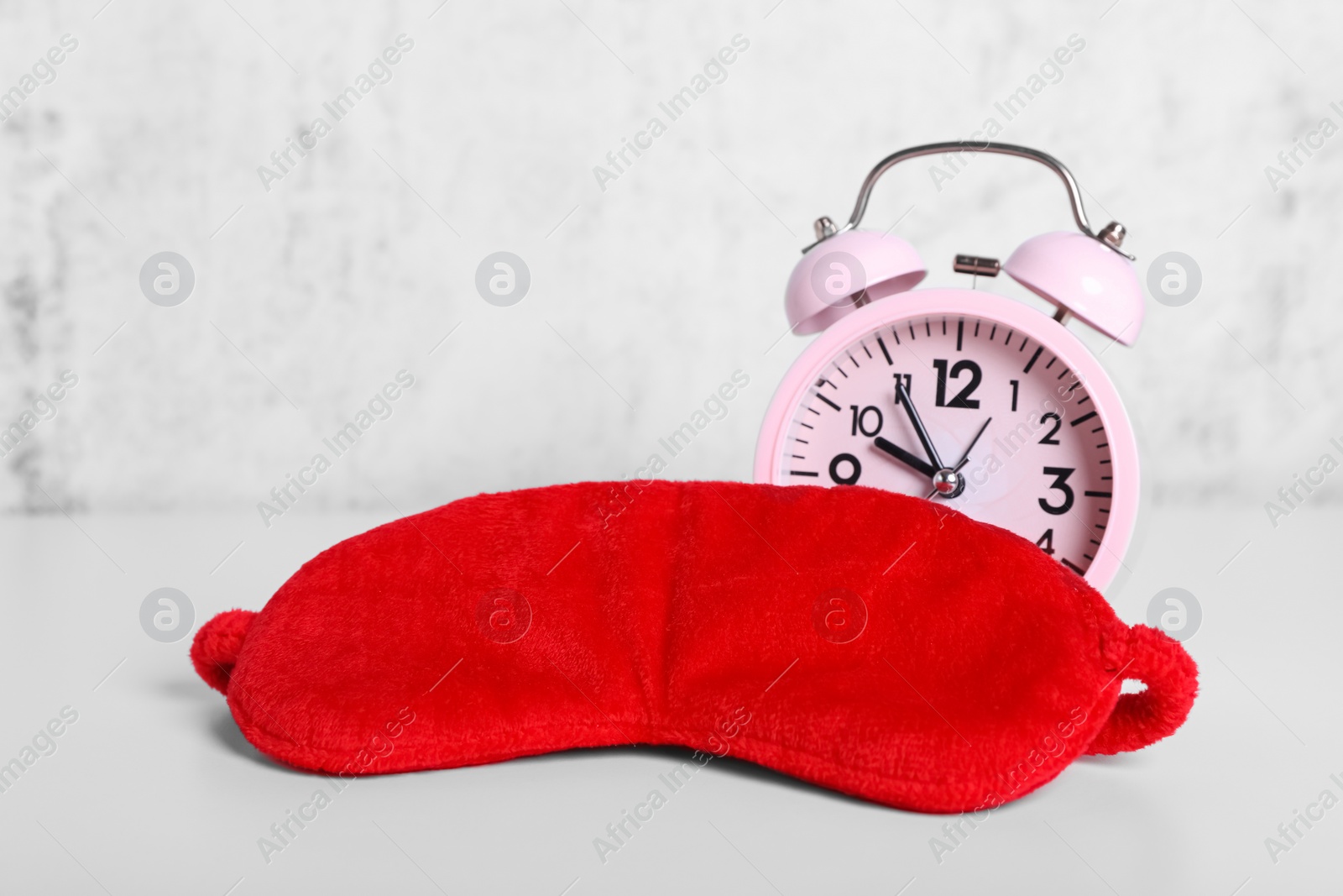 Photo of Red sleep mask and alarm clock on white table. Space for text