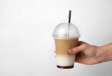 Woman holding plastic cup with caramel macchiato on light background