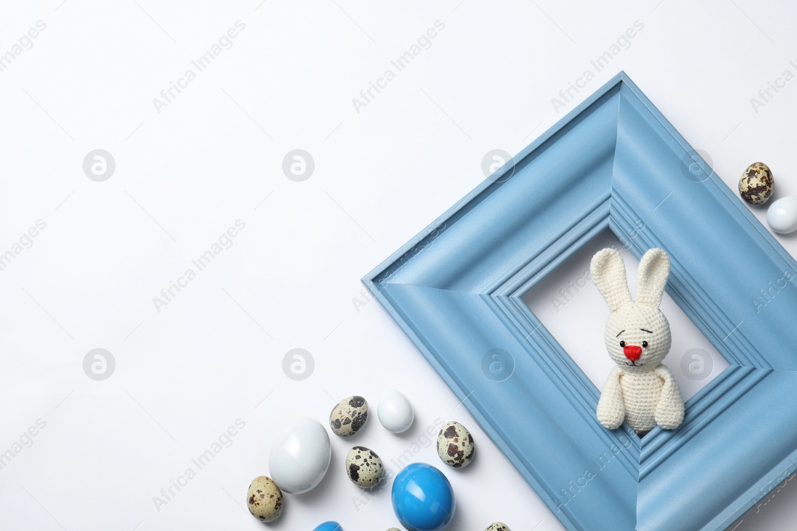 Photo of Easter bunny toy looking out wooden frame and eggs on white background, top view