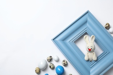 Photo of Easter bunny toy looking out wooden frame and eggs on white background, top view