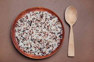 Composition with mixed brown and other types of rice in plate on color background, top view
