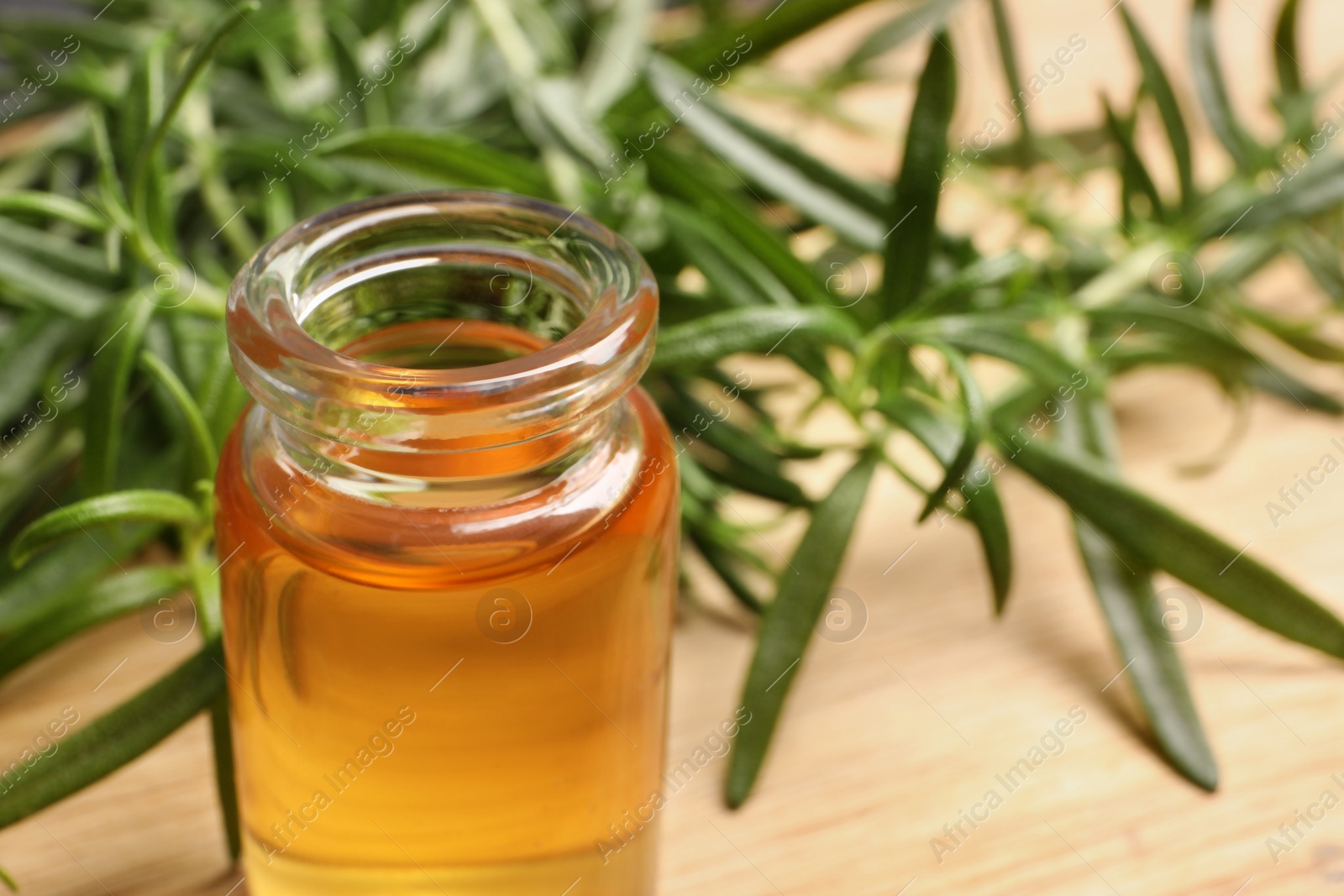 Photo of Bottle of essential oil and fresh rosemary sprigs on table, closeup