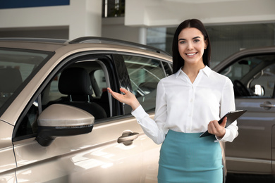 Photo of Saleswoman with clipboard near car in dealership