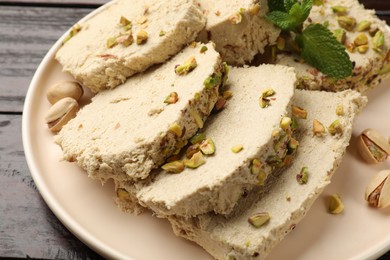 Photo of Pieces of tasty halva with pistachios and mint on table, closeup