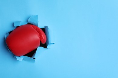 Photo of Man breaking through light blue paper with boxing glove, closeup. Space for text