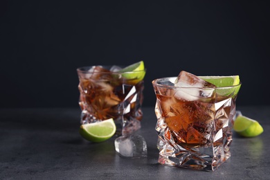 Glass of refreshing drink with ice cubes and lime on table against dark background. Space for text