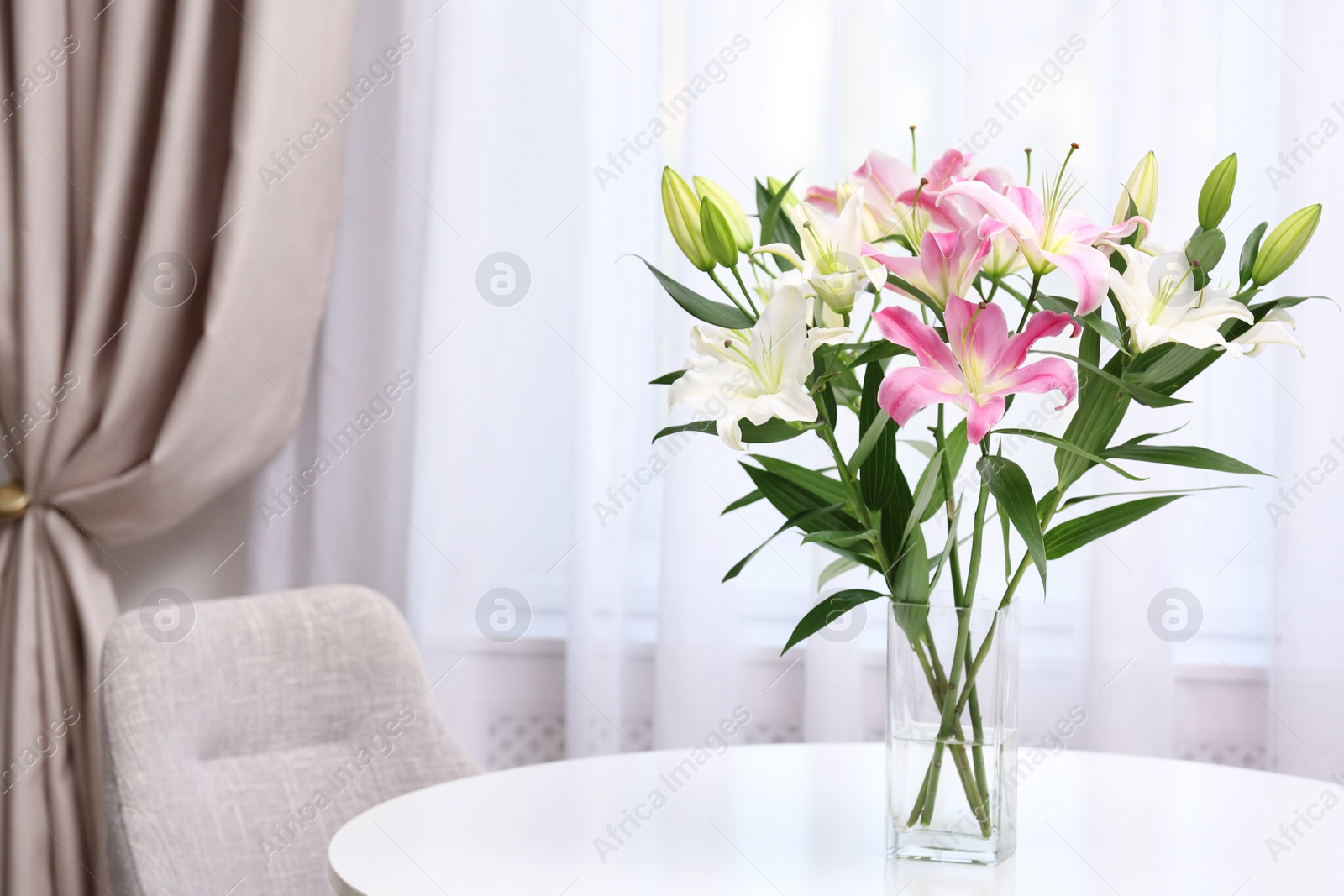 Photo of Vase with bouquet of beautiful lilies on white table indoors. Space for text