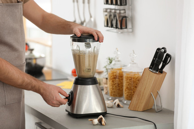 Young man using blender to cook cream soup in kitchen, closeup